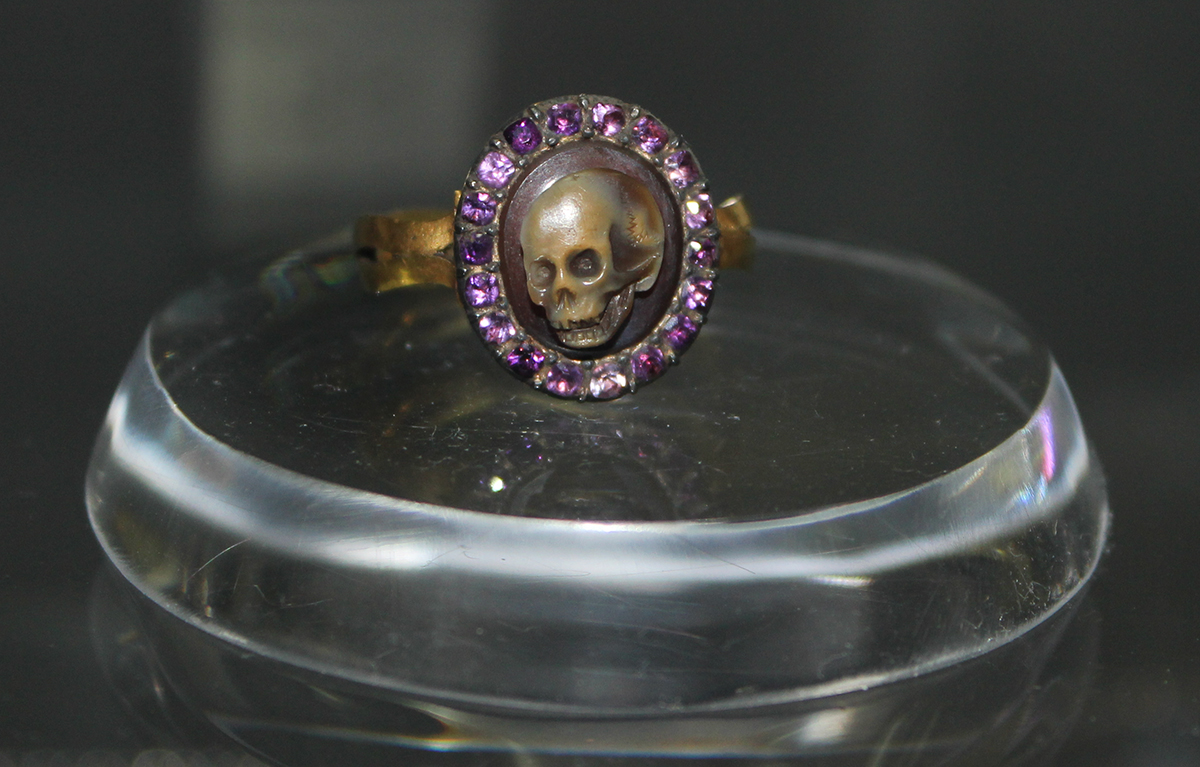 A close up of a ring with a carved skull and amethysts.