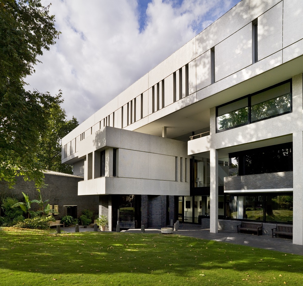 Side view of the RCP shwoing a white tield building with slit windows ont e htop floor, large glazing below wit ha box-like room jutting out over the garden.