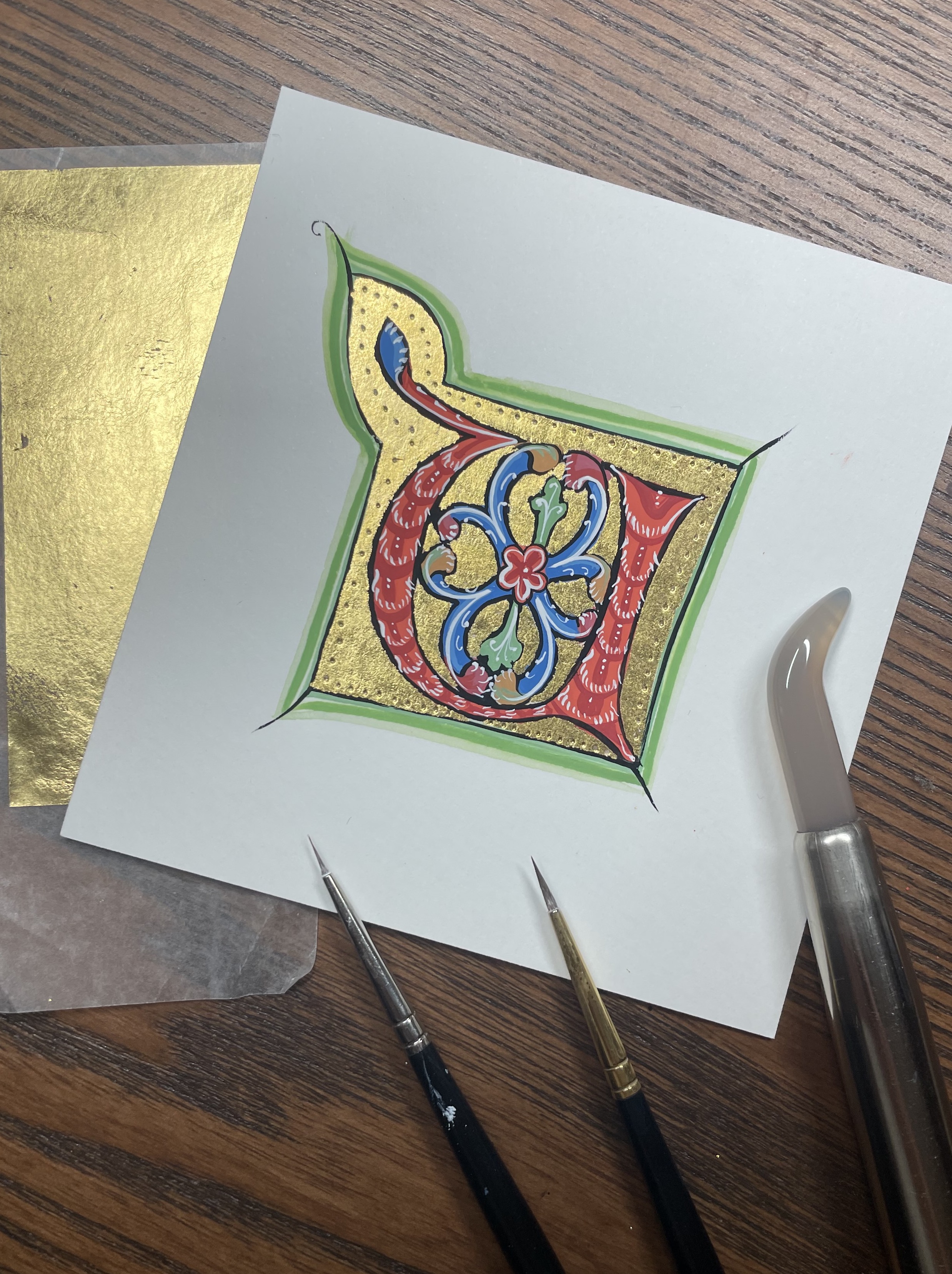 An illuminated letter on paper and several brushes.