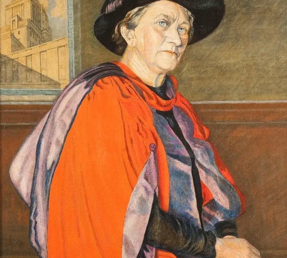Dorothy Christian Hare, an older woman dressed in orange and purple robes looks down at the viewer. Dorothy Christian Hare, an older woman dressed in orange and purple robes looks down at the viewer.