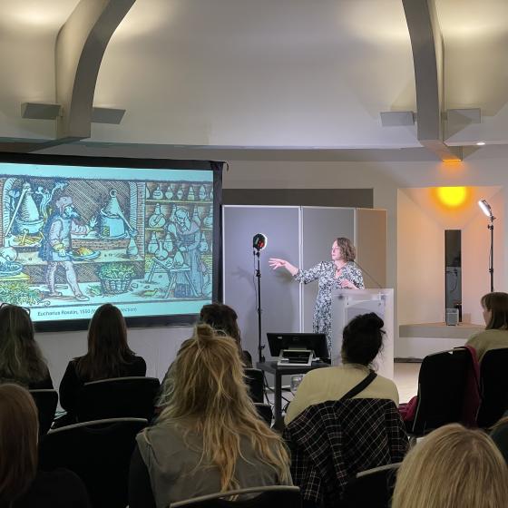 Dr Lisa Smith lecturing with a colourful illustrated slideshow. Dr Lisa Smith lecturing with a colourful illustrated slideshow.